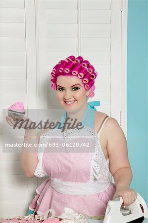 Portrait of happy young woman holding cupcake while ironing