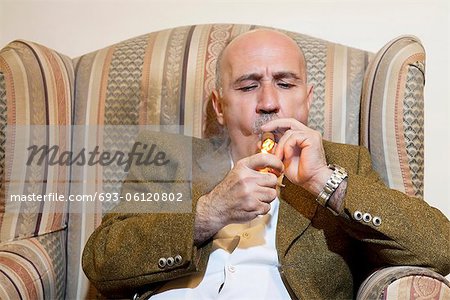 Älterer Mann Anzünden der Zigarre sitzen auf Sessel