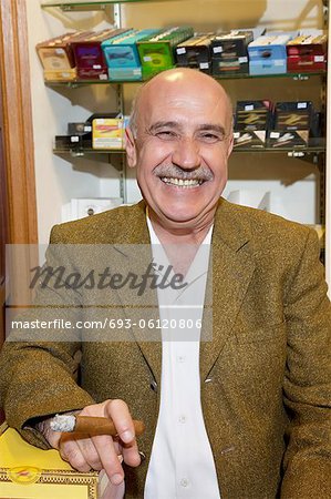 Portrait of a happy mature owner of tobacco shop smoking cigar