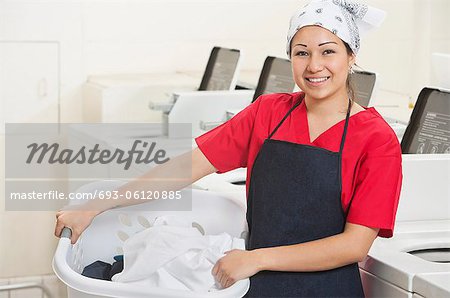 Portrait d'une heureuse jeune employée transportant un panier à linge avec machines à laver en arrière-plan