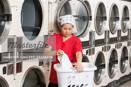 Young female employee carrying laundry basket with washing machines in background