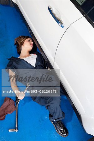 Woman lying down on floor working on car in automobile garage