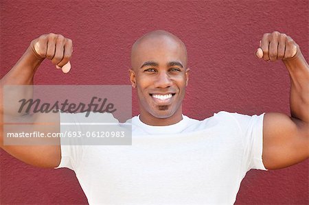 Portrait d'un homme afro-américain heureux flexing muscles sur fond coloré