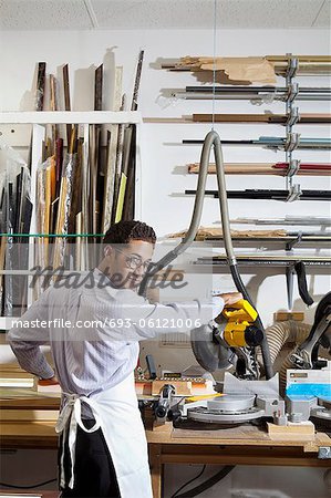 Portrait of a young man looking back while using circular saw in workshop