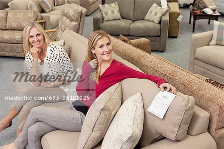 Portrait of happy mother and daughter sitting on sofa in furniture store