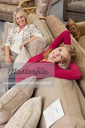 Portrait de la fille de détente sur le canapé tandis que la mère à la recherche dans le magasin de meubles