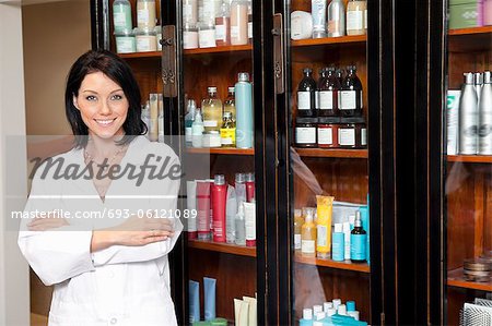 Portrait d'un employé de salon de beauté debout avec les bras croisés et cosmétiques en arrière-plan