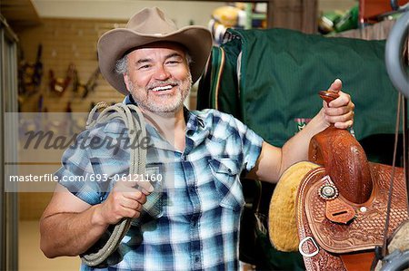 Happy mature cowboy with saddle and rope in feed store