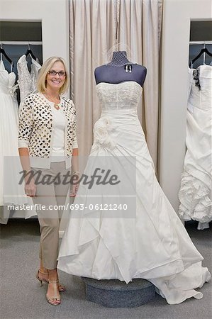 Portrait of a happy woman standing by elegant bridal dress in boutique