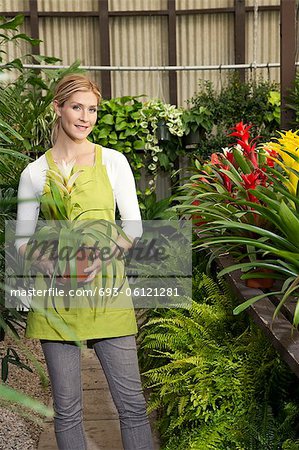 Portrait of a happy young woman standing with potted plant in greenhouse