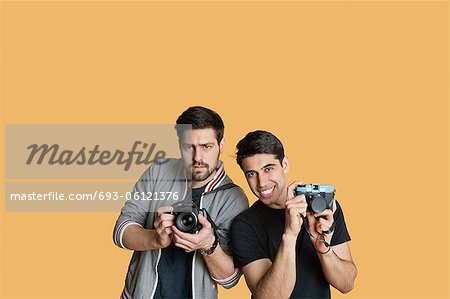 Portrait of young male friends with digital camera over colored background