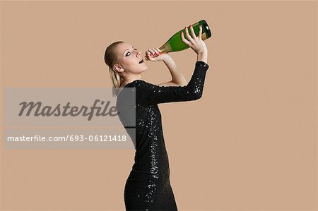 Portrait of beautiful young woman drinking champagne from bottle over colored background