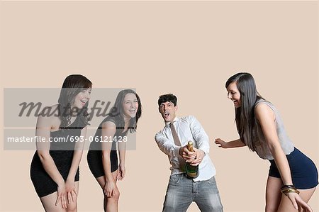 Young friends opening champagne bottle over colored background