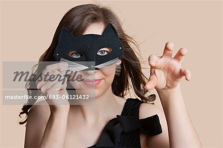 Portrait of a young woman looking through eye mask imitating as cat over colored background