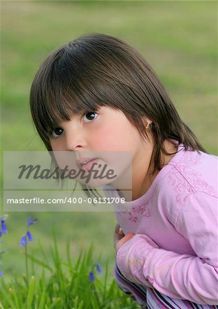 Face of a little girl sitting on the grass next to some bluebells.