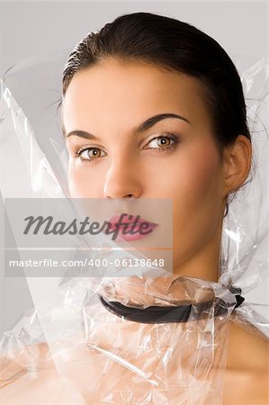 beauty portrait of young brunette with red lips and cellophane around her face, she is slightly turned of three quarters at right and looks in to the lens