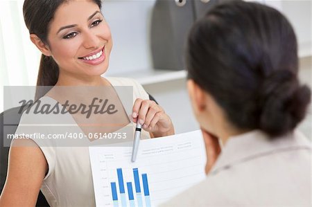 Beautiful young Latina Hispanic woman or businesswoman in smart business suit sitting at a desk using a graph at an office meeting