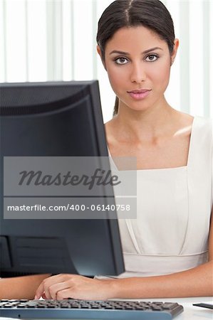 Beautiful young Latina Hispanic woman or businesswoman in smart business suit sitting at a desk in an office using a computer