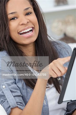 Beautiful happy young African American woman or girl smiling and using a tablet computer at home on her sofa