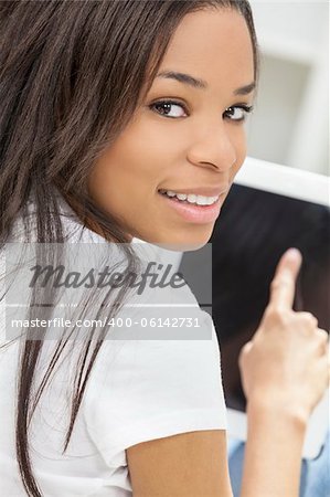 Beautiful happy young African American woman or girl smiling and using a tablet computer at home on her sofa