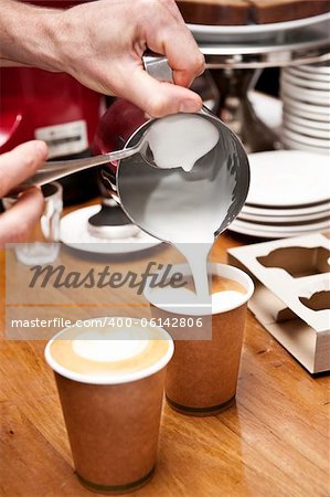 a barista pours milk to complete the coffee making process, creating a love heart shape in the milk. (no brand names on grinder or cups)