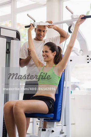 People and sports, man at work as personal trainer and helping young female athlete exercising in fitness gym