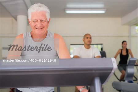People and sports, elderly man working out on treadmill in fitness gym among young people