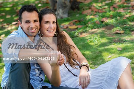 Happy beautiful young man and woman in love, lying on grass in park and relaxing