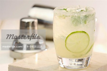 A mojito in a glass in front of a cocktail shaker