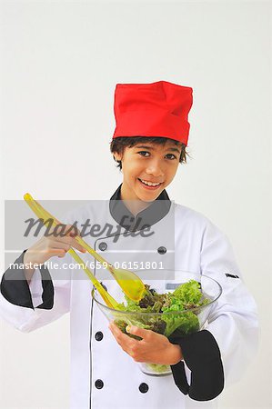 Un garçon habillé comme un chef mélange de salade
