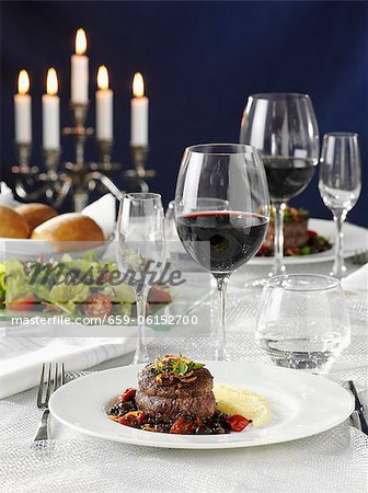 Beef medallions with vegetables, salad and red wine on a laid table