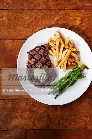 Steak vom Grill mit Pommes frites und grünen Bohnen auf einem weißen Teller; Von oben