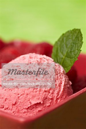 Une boule de glace framboise avec une feuille de menthe et de framboises fraîches