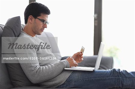L'homme tenant une carte de crédit et à l'aide d'un ordinateur portable L'homme tenant une carte de crédit et à l'aide d'un ordinateur portable