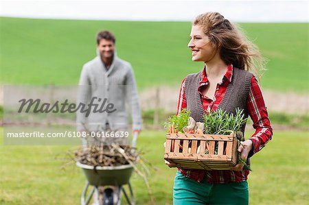 Woman holding a basket of vegetables with her husband collecting firewood
