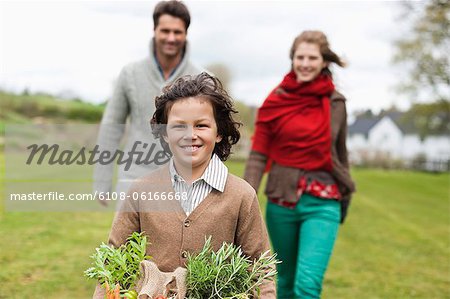 Portrait d'un garçon tenant un panier de légumes avec ses parents dans une ferme