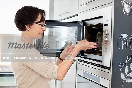 Elderly woman putting a tray into an oven