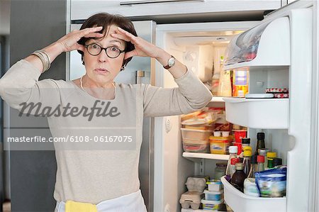 Porträt einer älteren Frau schockiert vor einem Kühlschrank suchen