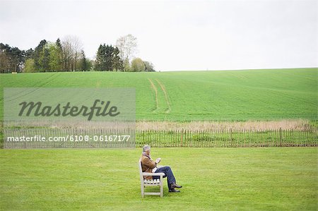 L'homme assis sur le banc et à l'aide d'un téléphone mobile dans un champ