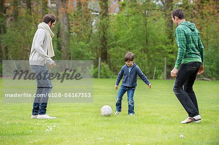 Garçon jouant au soccer avec deux hommes dans un parc
