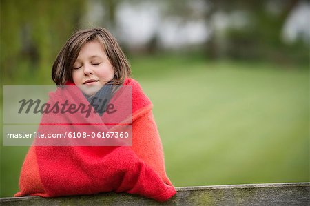 Girl wrapped in a blanket with her eyes closed in a farm