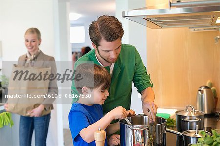 Boy and his father cooking in the kitchen while mother carrying a grocery bag
