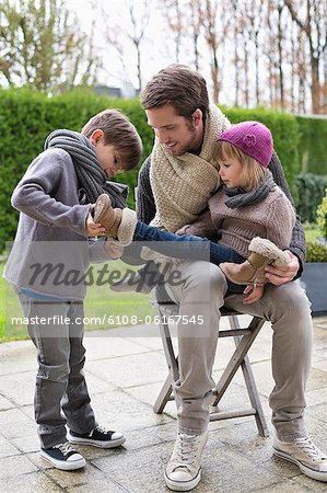 Garçon chausser les chaussures sa sœur assise sur les genoux de son père