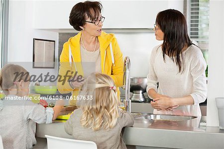 Two girls with her mother and grandmother discussing in a kitchen