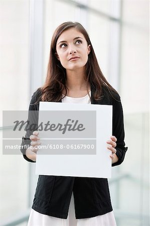 Femme tenant une pancarte blanche et penser dans un bureau