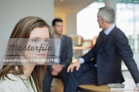 Female executive thinking in an office with her colleagues discussing in the background