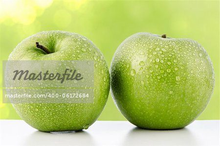 Two fresh green apples on green defocused background.