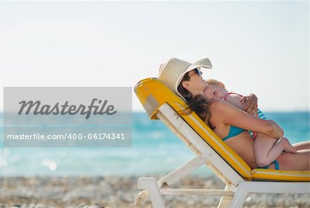 Mother with baby laying on sunbed on beach