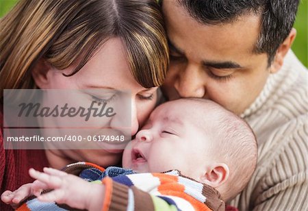 Happy Mixed Race Parents Hugging Their Son in the Park.