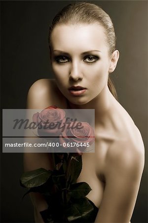 pretty blonde girl's low key portrait with three red roses, she is in front of the camera, looks in to the lens and takes the roses on her breast